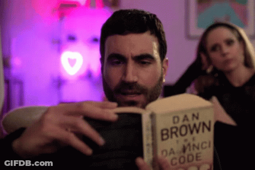 A Man Reading A Book By Dan Brown GIF