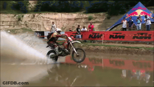 A Man Riding A Dirt Bike In The Water With A Ktm Sign In The Background GIF