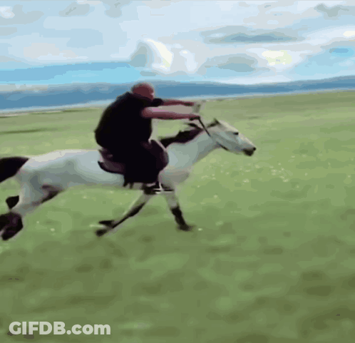 A Man Riding A Horse In A Field With Mountains In The Background GIF