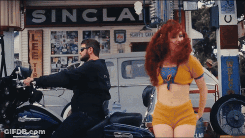 A Man Riding A Motorcycle Next To A Woman In Front Of A Sinclair Sign GIF