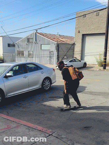 A Man Riding A Skateboard Down A Street With A Bag On His Back GIF