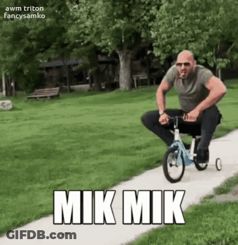 A Man Riding A Tricycle On A Sidewalk With Mik Mik Written On The Side GIF