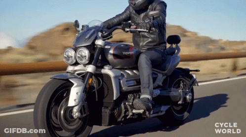 A Man Riding A Triumph Motorcycle On The Road GIF