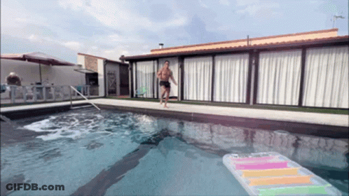 A Man Runs Into A Swimming Pool With A Raft In The Water GIF