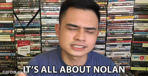 A Man Says It 'S All About Nolan In Front Of A Stack Of Books GIF