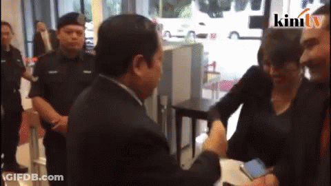 A Man Shaking Hands With A Woman In Front Of A Sign That Says ' Kimi Tv ' GIF