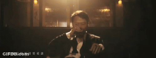 A Man Singing Into A Microphone In A Dark Room With Chinese Writing On The Bottom GIF