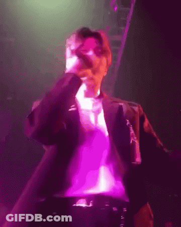 A Man Singing Into A Microphone In A Purple Light GIF