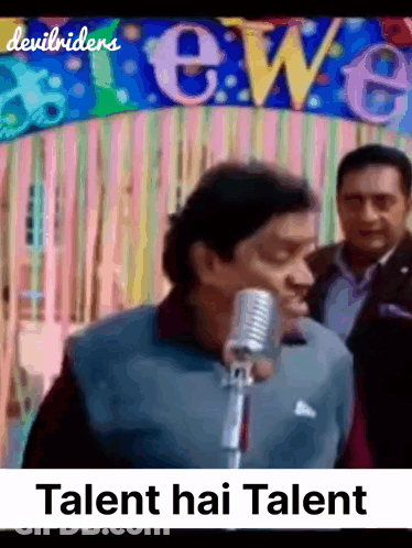 A Man Singing Into A Microphone In Front Of A Banner That Says Talent Hai Talent GIF