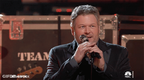 A Man Singing Into A Microphone In Front Of A Box That Says Team GIF