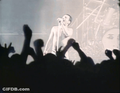 A Man Singing Into A Microphone In Front Of A Crowd Of People GIF