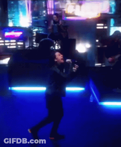A Man Singing Into A Microphone In Front Of A Crowd GIF