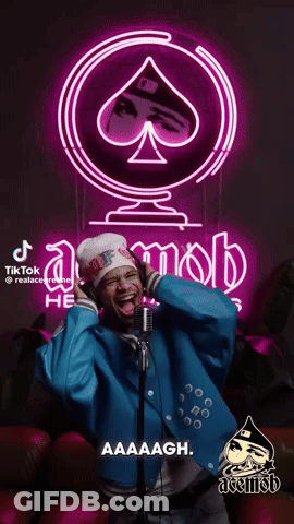 A Man Singing Into A Microphone In Front Of A Neon Sign That Says Acemob GIF