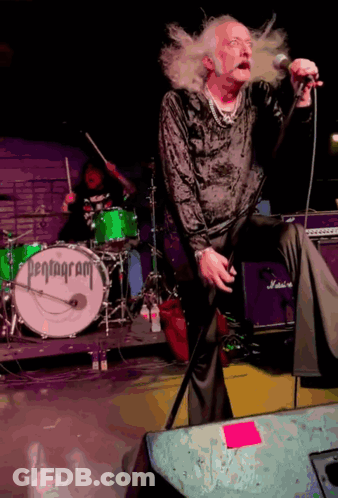 A Man Singing Into A Microphone In Front Of A Pentagram Drum GIF