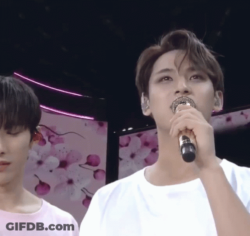 A Man Singing Into A Microphone In Front Of A Pink Background GIF