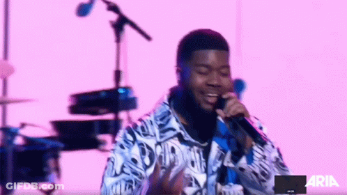 A Man Singing Into A Microphone In Front Of A Pink Background With The Word Aria On It GIF