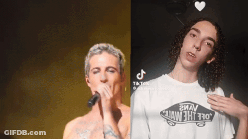 A Man Singing Into A Microphone Next To Another Man Wearing A White Vans Shirt GIF