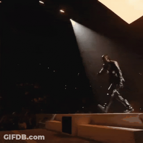 A Man Singing Into A Microphone On A Stage GIF