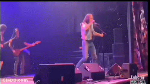 A Man Singing Into A Microphone On A Stage With Carlos Live Written On The Bottom Right GIF