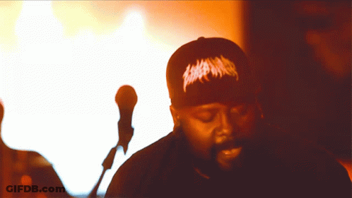 A Man Singing Into A Microphone Wearing A Black Hat That Says ' Slayer ' On It GIF