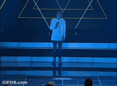 A Man Singing Into A Microphone Wearing A Hat And Glasses GIF