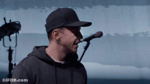A Man Singing Into A Microphone Wearing A Hat GIF