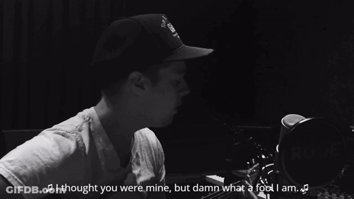 A Man Singing Into A Microphone Wearing A Hat That Says Gibson GIF