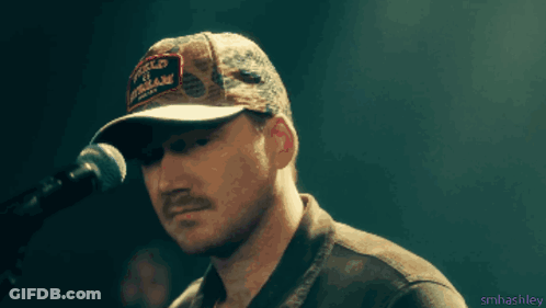 A Man Singing Into A Microphone Wearing A Hat That Says " World Of Motorcycles " GIF