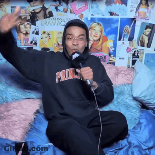 A Man Singing Into A Microphone Wearing A Prince Hoodie GIF