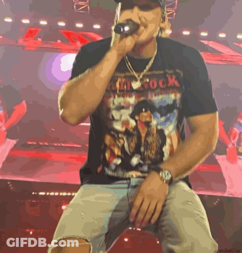 A Man Singing Into A Microphone Wearing A Shirt That Says ' My Rock ' GIF