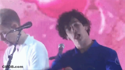 A Man Singing Into A Microphone While Another Man Looks On GIF