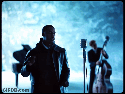 A Man Singing Into A Microphone While Another Man Plays A Bass GIF