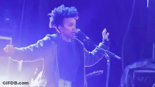 A Man Singing Into A Microphone While Another Man Plays A Bass Guitar GIF