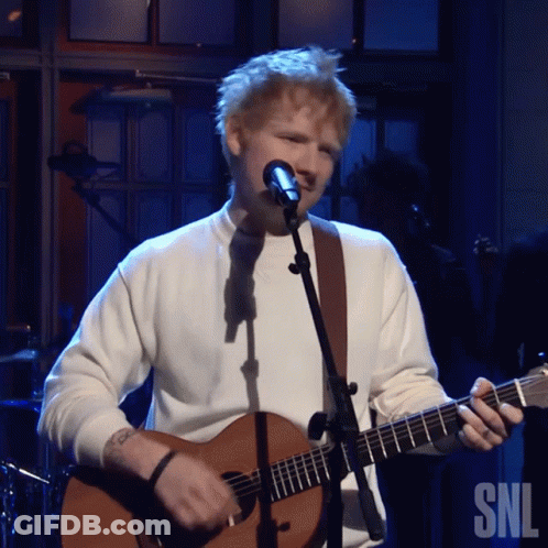 A Man Singing Into A Microphone While Holding A Guitar In Front Of A Snl Logo GIF