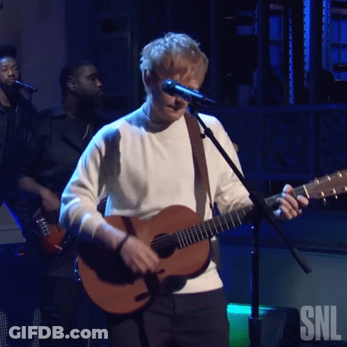 A Man Singing Into A Microphone While Holding A Guitar With The Snl Logo In The Background GIF