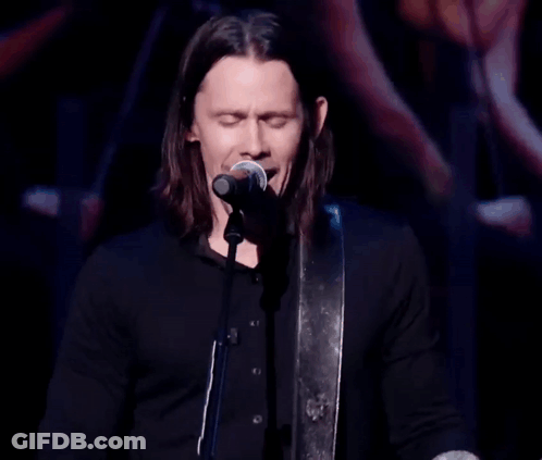 A Man Singing Into A Microphone While Playing A Guitar GIF