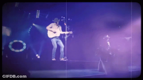 A Man Singing Into A Microphone While Playing A Guitar GIF