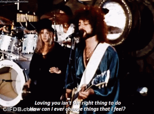 A Man Singing Into A Microphone While Playing A Guitar And A Woman Stands Behind Him GIF