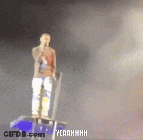 A Man Singing Into A Microphone While Standing On A Stage With Yeahhhh Written Below Him GIF