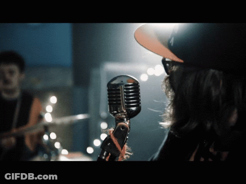 A Man Singing Into A Microphone With A Hat That Says La On It GIF