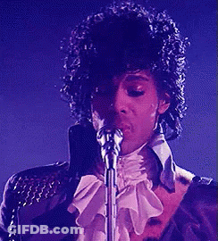 A Man Singing Into A Microphone With A Purple Background GIF