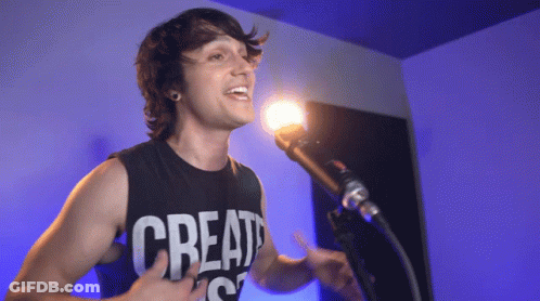 A Man Singing Into A Microphone With A Shirt That Says Create GIF