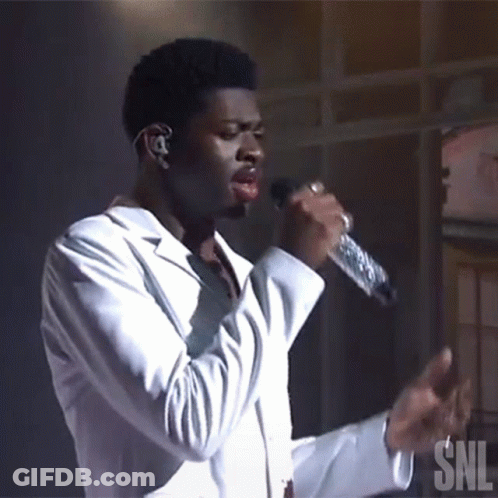 A Man Singing Into A Microphone With A Snl Logo In The Background GIF