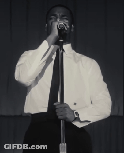A Man Singing Into A Microphone With A Watch On His Wrist GIF