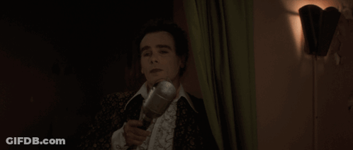 A Man Singing Into A Microphone With His Mouth Open GIF