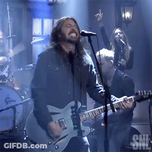 A Man Singing Into A Microphone With The Letters Snl Visible In The Background GIF
