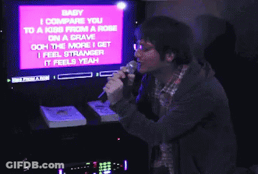 A Man Singing Into A Microphone With The Words Baby I Compare You To A Kiss From A Rose On The Screen Behind Him GIF