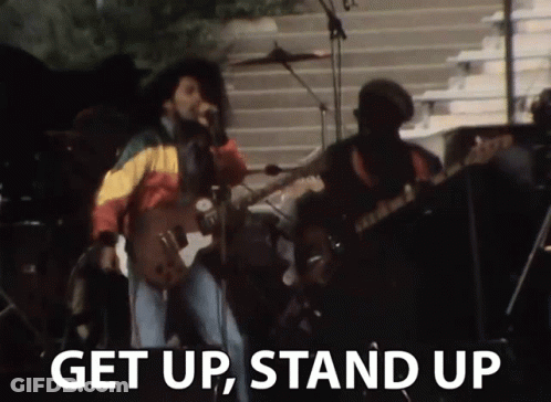 A Man Singing Into A Microphone With The Words " Get Up Stand Up " Next To Him GIF
