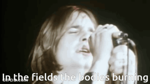 A Man Singing Into A Microphone With The Words In The Fields The Bodies Burning Above Him . GIF