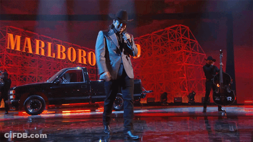 A Man Singing On Stage In Front Of A Sign That Says Marlboro GIF